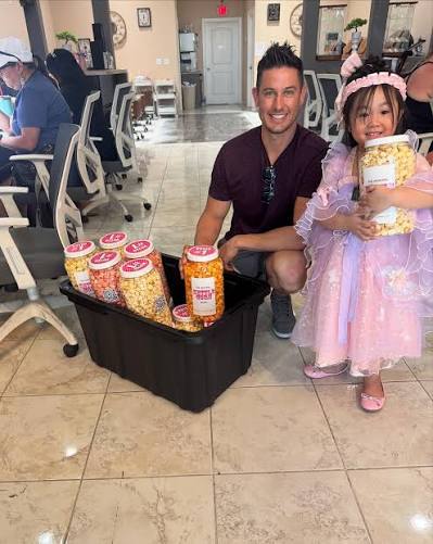An adult beside a child in a pink costume holding a jar of kettle corn.